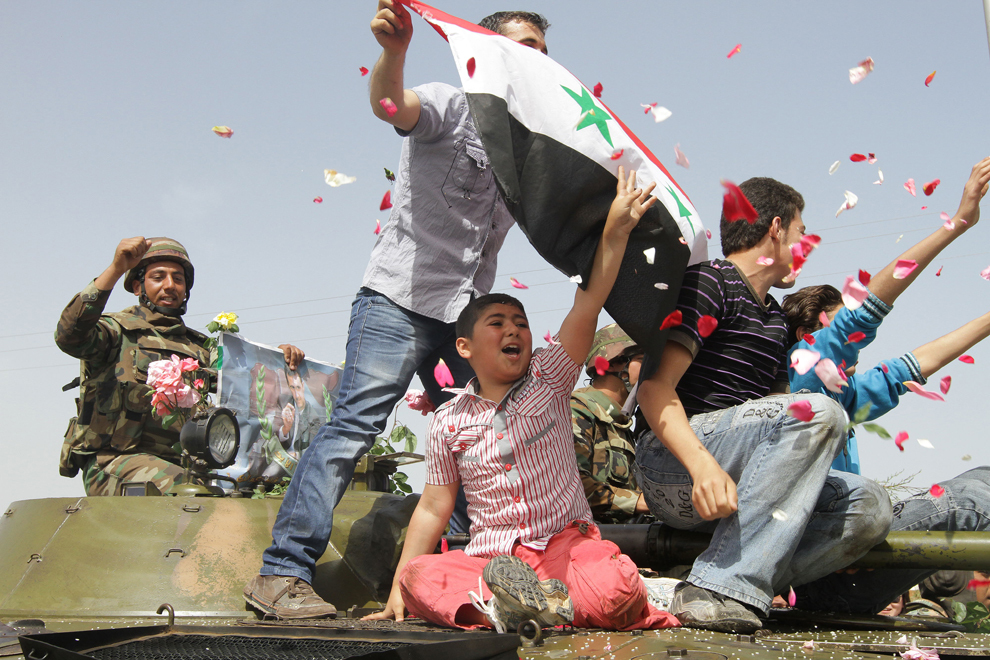 Femei siriene aruncă petale de trandafiri şi orez asupra soldaţilor guvernamentali, în timp ce tineri flutură un steag al Siriei pe un tanc militar care se retrage din centrul sudic al protestelor, Daraa, joi, 5 mai 2012. (Louai Beshara / AFP)