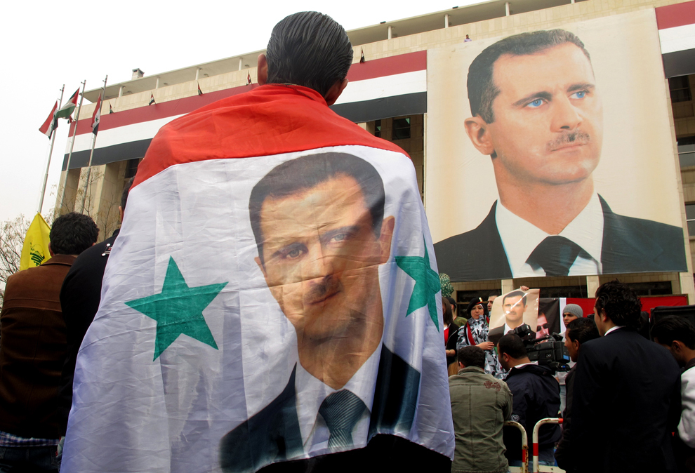Un sirian poartă drept capă steagul naţional cu portretul preşedintelui Bashar Al-Assad în timpul unei demonstraţii organizate in sprijinul liderului şi a armatei siriene, in Damasc, marţi, 14 februarie 2012. (Patrick Baz / AFP)