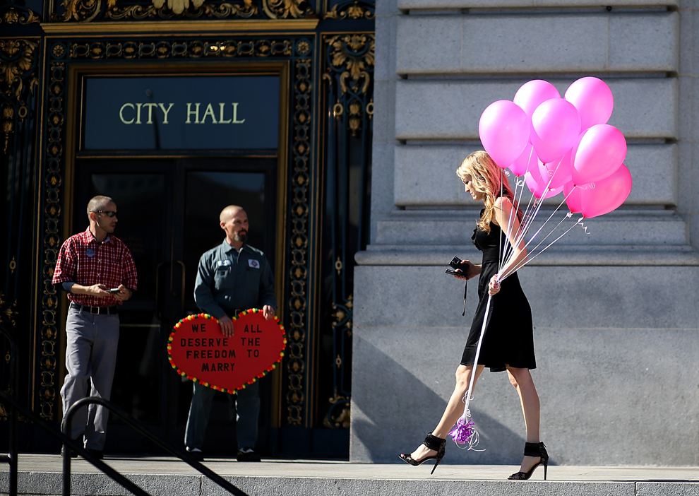 Frank Capley (C) şi Joe Alfano (S),  un cuplu de homosexuali din San Francisco, privesc o femeie care ţine în mână baloane roz, în faţa primăriei, joi, 14 februarie 2013. 