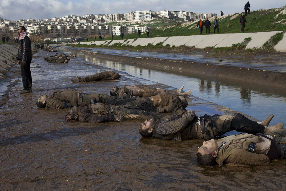 Un sirian stă lângă corpurile unor bărbaţi executaţi pe malul unui canal din oraşul sirian Alep, marţi, 29 ianuarie 2013. Corpurile a 68 de bărbaţi si copii executaţi cu un foc de armă în cap au fost găsite in râul Quweiq. 