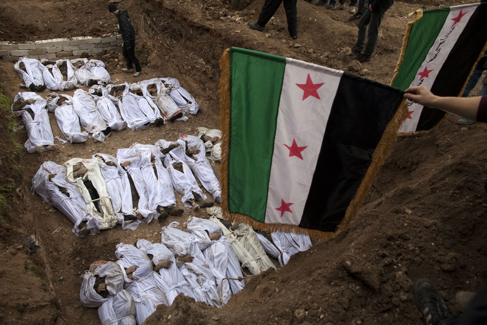 Persoane îndoliate flutură steagul Siriei pre-Baath, folosit acum de Armata Siriană Liberă, deasupra corpurilor civililor executaţi si aruncaţi în râul Quweiq, în timpul ceremoniei de înmormântare, joi, 31 ianuarie 2013. (JM Lopez / AFP)