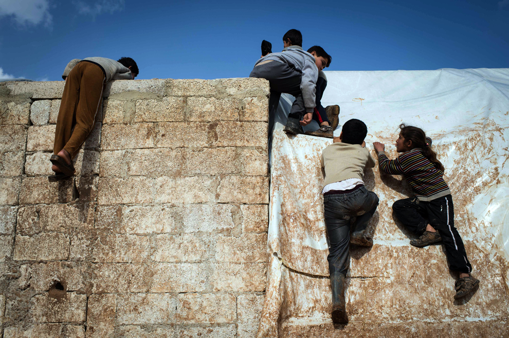 Copii refugiaţi sirieni, dislocaţi în interiorul ţării, într-o tabără de refugiaţi din oraşul Azaz, în apropierea graniţei cu Turcia, escaladează un zid, duminică, 10 februarie 2013. (Elias Edouard / AFP)
