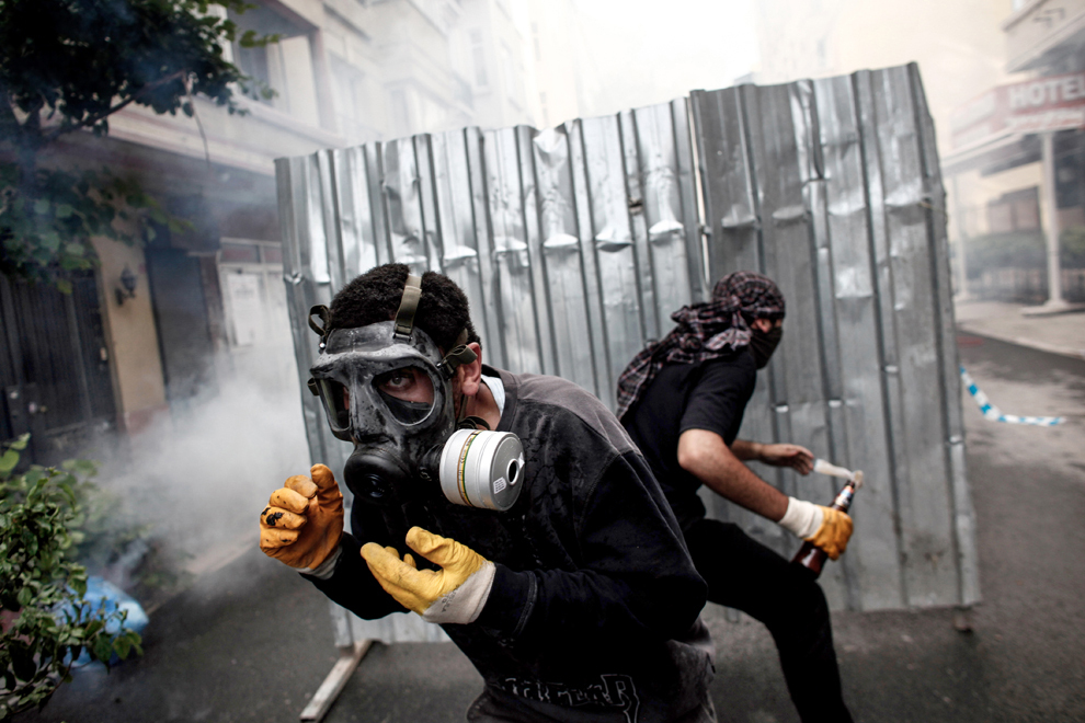 Demonstranţi purtând măşti de gaze se adăpostesc în spatele unei baricade, în timpul ciocnirilor dintre forţele de ordine şi manifestanţi, în Piaţa Taksim din Istanbul, marţi, 11 iunie 2013.  