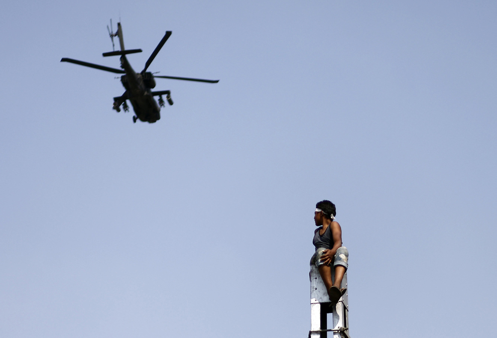 Un suporter al opoziţiei egiptene ce stă pe un stâlp priveşte către un elicopter militar ce survolează o piaţă din Cairo, Egipt, marţi, 2 iulie 2013. 