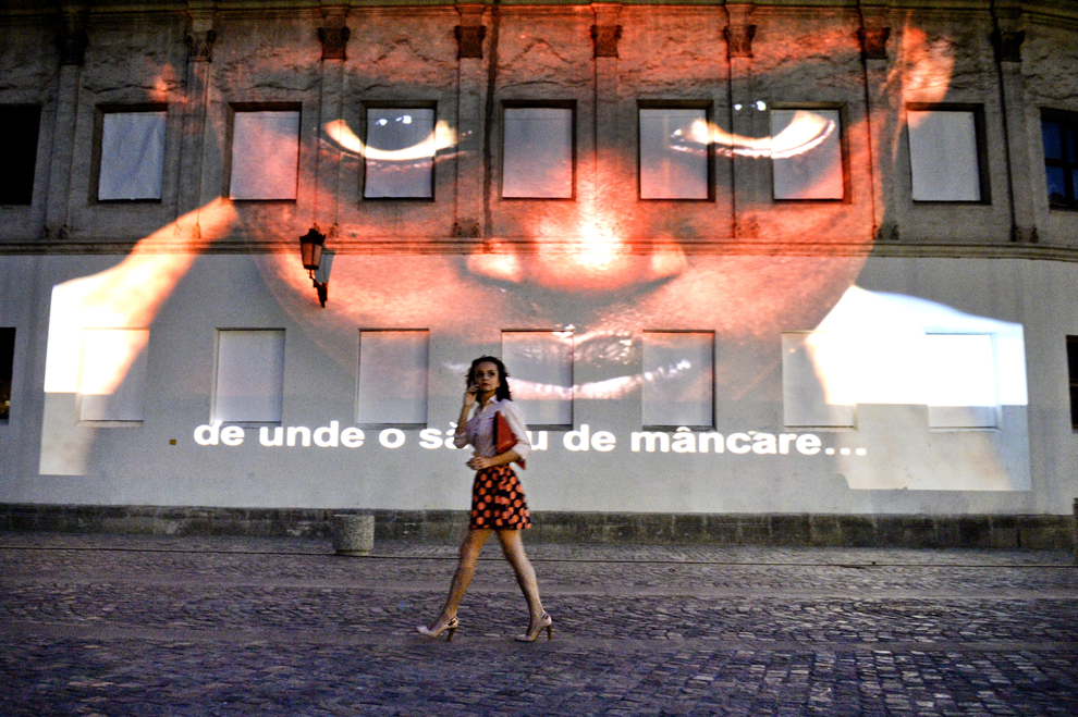 O tânără trece prin faţa unor mesaje proiectate pe peretele Hanului Manuc, în cadrul unui proiect artistic multimedia intitulat „Refugiu şi subzistenţă“, în Bucureşti, joi, 20 iunie 2013.
