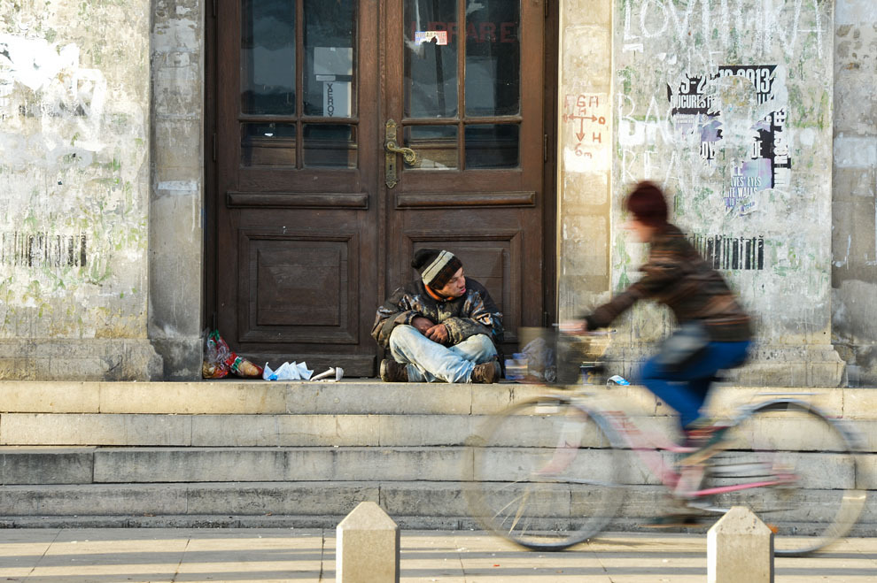 O biciclistă trece pe lângă un om al străzii, ce stă pe treptele Universităţii din Bucureşti, duminică, 16 februarie 2014.