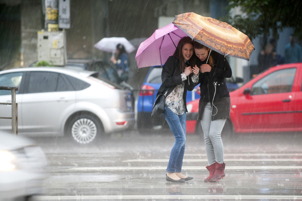 Două tinere se adăpostesc sub umbrele în timp ce aşteaptă să traverse Şoseaua Mihai Bravu în timpul unei ploi torenţiale de vară, în Bucureşti, vineri, 20 iunie 2014.