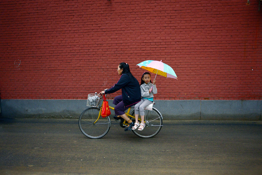 O fetiţă ce ţine în mână o umbrelă este transportată pe o bicicletă în Beijing, marţi, 2 septembrie 2014.