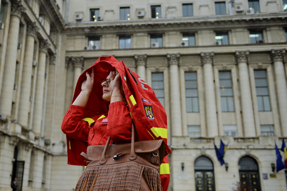 O femeie, care se fereşte de ploaie cu o haină din echipamentul SMURD, pleacă de la sediul MAI, după ce a participat la ceremonia de sărbătorire a 10 ani de operare aero-medicală SMURD, în Bucureşti, marţi, 7 octombrie 2014.