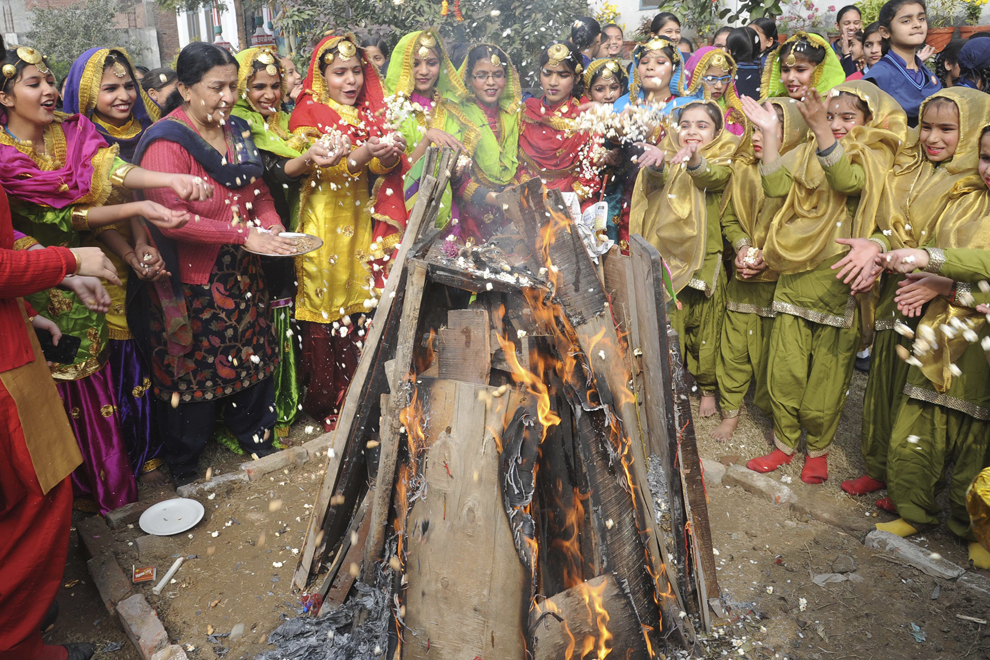 Eleve din India îmbrăcate în costume tradiţionale Punjabi aruncă orez, alune şi floricele de porumb într-un foc, în ajunul sărbătorii Amritsar, luni 12 ianuarie 2015.