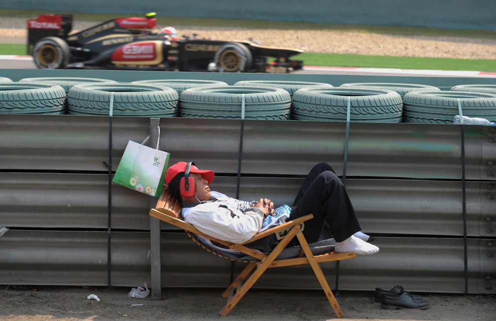 Un angajat responsabil cu siguranţa pe pistă doarme în timp ce pilotul finlandez al echipei Lotus, Kimi Raikkonen (în fundal), trece pe lângă el, în a doua sesiune de antrenamente a Marelui Premiu de Formula 1 al Chinei, în Shanghai, vineri, 12 aprilie 2013. 