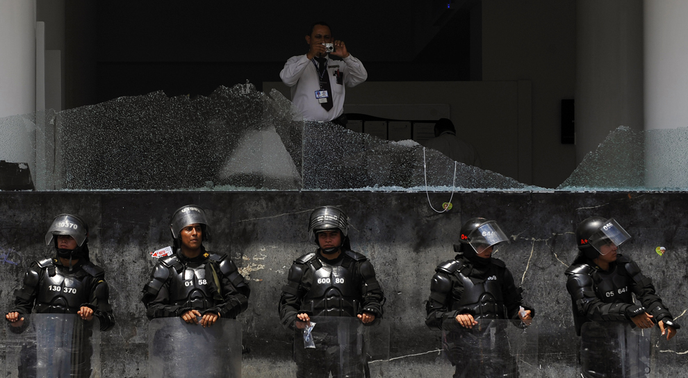 Un bărbat fotografiază în timp ce poliţişti păzesc o clădire guvernamentală deteriorată, în timpul unui protest organizat cu ocazia Zilei Internaţionale a Muncitorilor, în Bogota, Columbia, duminică, 1 mai 2011.  