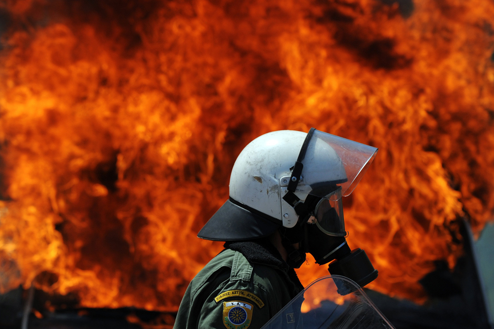 Un scutier grec trece prin faţa unei dubiţe ce a luat foc dupa ce a fost lovită de un cocktail Molotov, în timpul unei demonstraţii, în Atena, Grecia, sâmbătă, 1 mai 2010. 