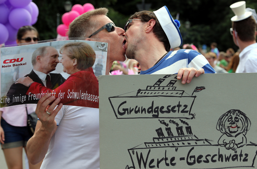Doi bărbaţi se sărută ţinând în mână o fotografie înfăţişându-i pe Vladimir Putin şi Angela Merkel cu textul “O prietenie puternică a doi homofobi”, în Berlin, sâmbătă, 22 iunie 2013. 