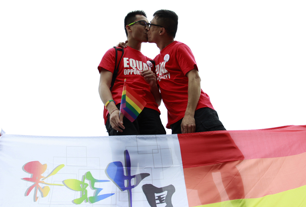 Doi barbaţi se sărută în spatele unui steag în culorile curcubeului, simbol al mişcării LGBT, în timpul unei parade anti-discriminare, în Changsha, provincia Hunan, vineri, 17 mai 2013. 