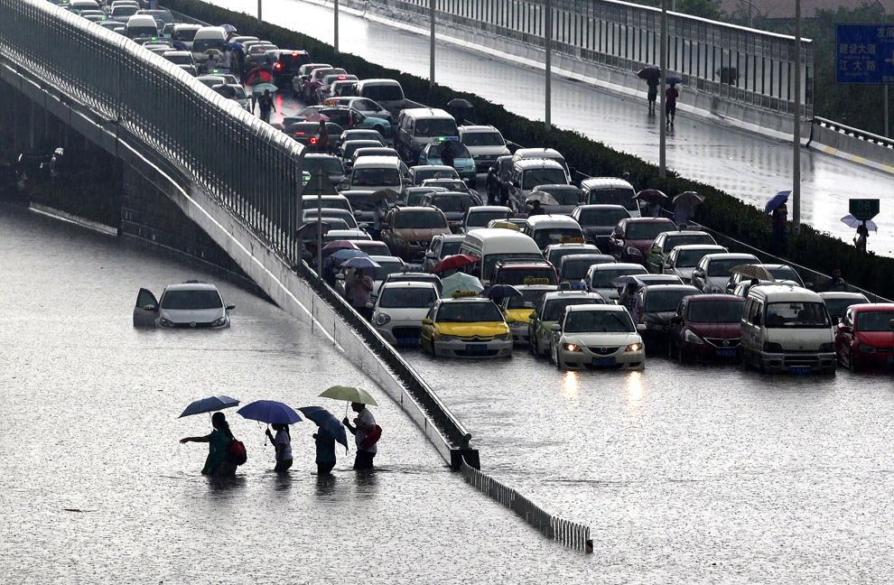 Oameni merg pe o stradă inundată, în Wuhan, provincia Hubei, după o furtună puternică, duminică, 7 iulie 2013. 