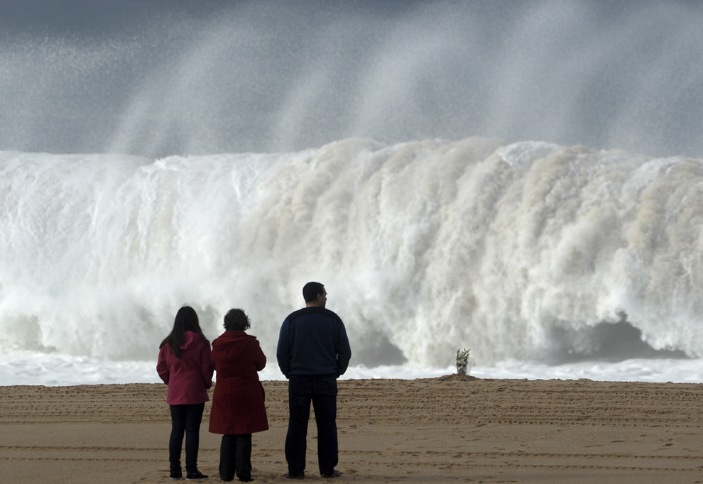 Flori sunt văzute pe plaja din Meco, lângă Sesimbra, marţi, 17 decembrie 2013, în timp ce mai mulţi oameni privesc valurile uriaşe. Un student a murit şi cinci persoane sunt date dispărute dupâ ce grupul în care se aflau a fost lovit de un val uriaş pe o plajă din Portugalia, duminică, 15 decembrie 2013.