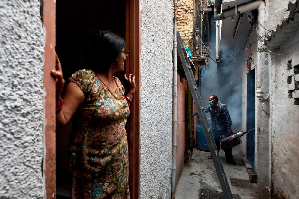 O femeie (S) priveşte un muncitor municipal în timpul unei acţiuni de fumigaţie împotriva ţânţarilor, într-un cartier din New Delhi, India, joi, 3 octombrie 2013.
