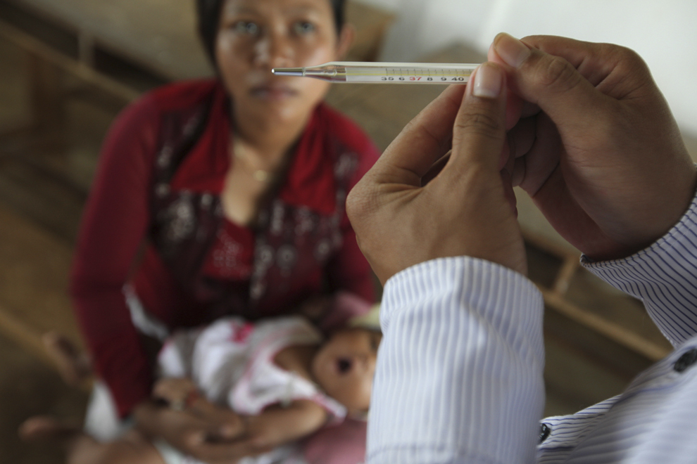 O femeie priveşte un medic ce ia temperatura unui copil, în timpul unui screening medical de malarie, organizat de Organizaţia Mondială de Sănătate, în Prey Mong Kol, Cambogia, sâmbătă, 17 iulie 2010.