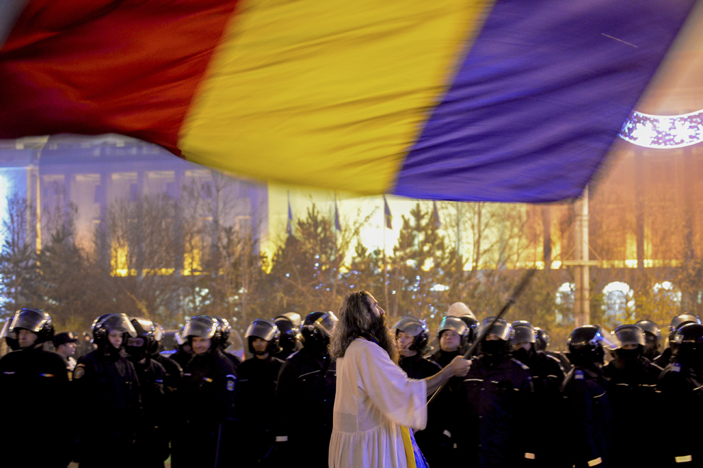 Un bărbat trece cu un drapel naţional prin faţa cordonului de jandarmi din faţa Guvernului, în timpul unui protest faţă de modificările aduse Codului penal, în Bucureşti, duminică, 15 decembrie 2013.
