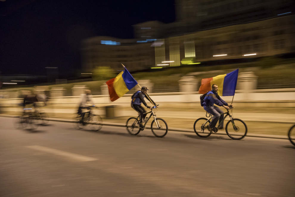 Doi biciclişti flutură steagul tricolor în timp ce trec prin faţa Palatului Parlamentului, în timpul unui protest faţă de proiectul minier de la Roşia Montană şi faţă de explorarea gazelor de şist, în Bucureşti, vineri, 6 septembrie 2013.