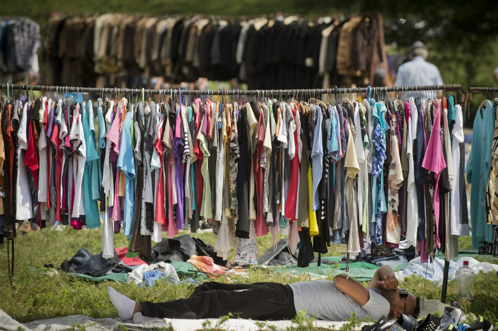 Un bărbat de etnie romă se odihneşte la umbra unui stativ cu haine second hand aduse pentru a fi vândute în timpul reuniunii anuale a romilor, cu ocazia sărbătorii Naşterii Maicii Domnului, în Costeşti, Vâlcea, luni, 8 septembrie 2014.