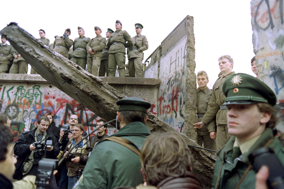 Doi poliţişti din vest germani împiedică accesul oamenilor printr-o porţiune căzuta a zidului Berlinului, în timp ce soldaţi din RDG sunt urcaţi pe porţiuni ale aceluiaşi zid, sâmbătă, 11 noiembrie 1989.
