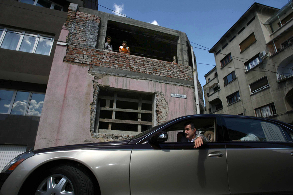Două persoane privesc de la etajul unei clădiri deteriorate maşina liderului PNG, Gigi Becali, în Bucureşti, marţi, 5 septembrie 2006. 