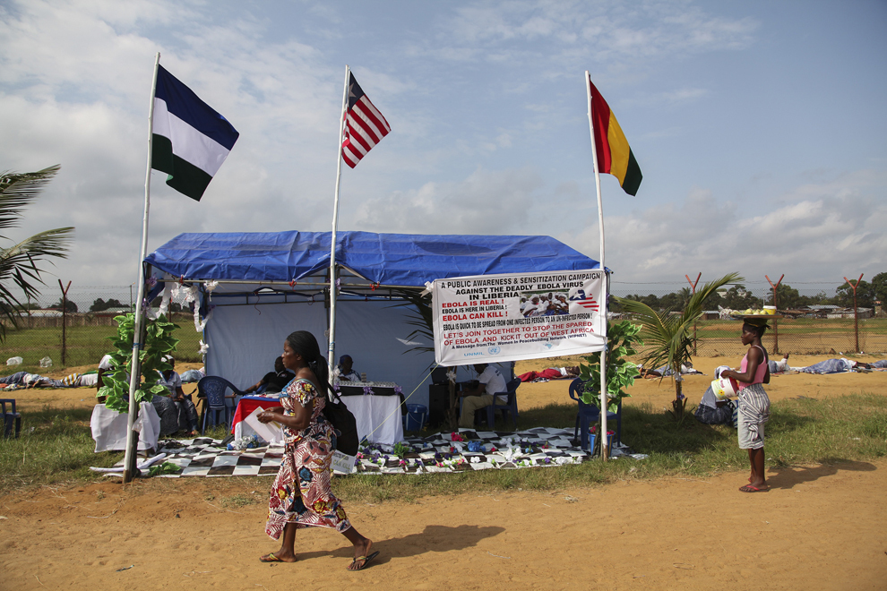 Femei trec pe lângă un cort al organizaţiei “The Liberian Women in Peace building Program (WIPNET)”, în Monrovia, Liberia, marţi, 5 august 2014. 