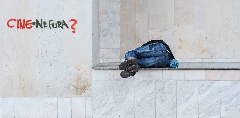 Un bărbat doarme la intrarea unui bloc, lângă un grafitti cu mesajul "Cine ne fură?", pe o stradă din Bucureşti, joi, 2 aprilie 2015.