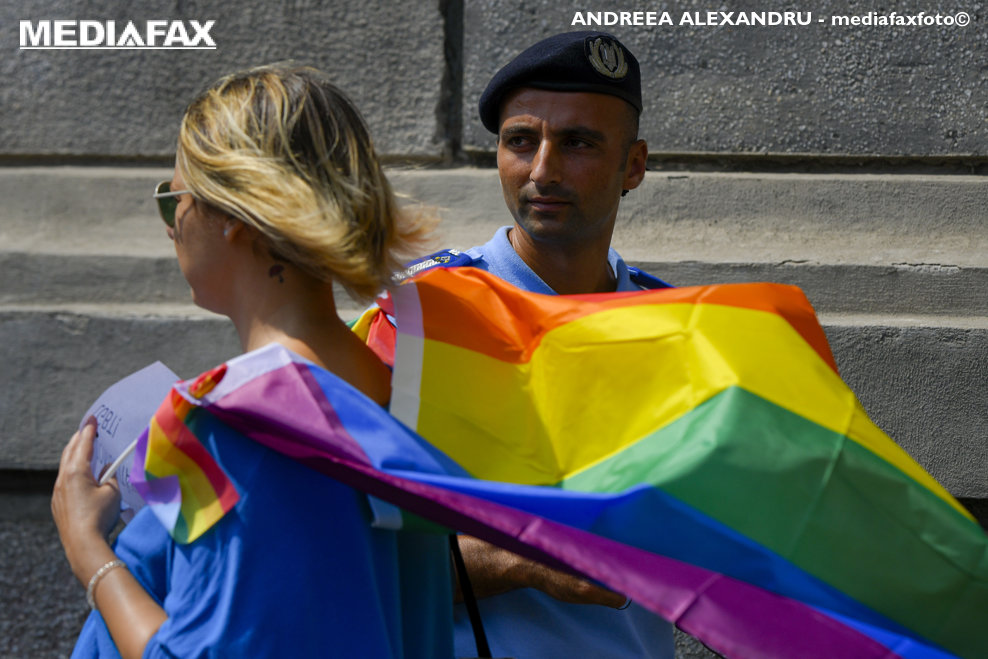 Un jandarm trece pe langa o tanara ce poarta pe umeri steagul curcubeu al comunitatii LGBTQIA+  in timpul protestului "NU Homofobiei la STB" organizat de MozaiQ, in fata sediului Societatii de Transport Bucuresti din Bucuresti, vineri, 13 august 2021. ANDREEA ALEXANDRU / MEDIAFAX FOTO