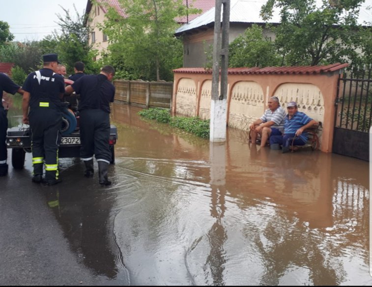 Imaginea articolului Fotografia zilei vine din Teleorman. Doi localnici stau pe bancă în timp ce pompierii scot apa din comună